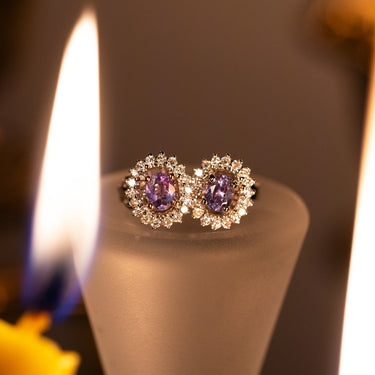 Natural Alexandrite stud earrings with diamond halo set in 18k white gold, showing purple gemstone color surrounded by brilliant diamonds.